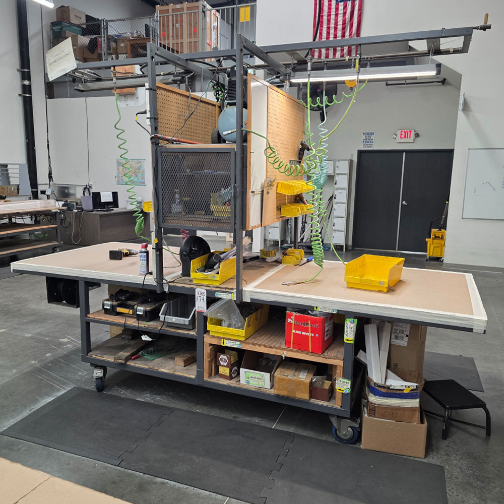 STEEL ASSEMBLY TABLE ON CASTERS, W/ 11' X 4' WOOD TOP, 37" TOP HT, W/ CENTER STORAGE & LIGHTS, CONTENTS NOT INCLUDED-174